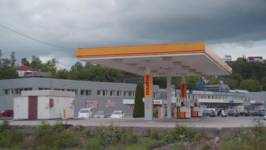 A gas station with white and orange colors and several cars parked behind it