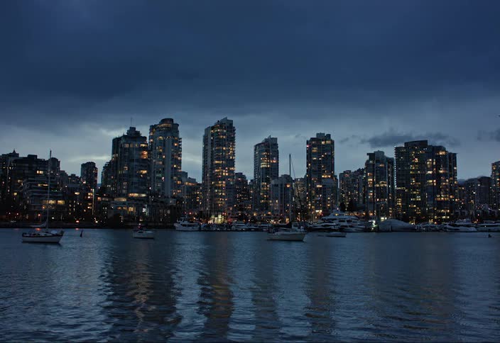 Boats are anchored in front of oceanside apartment buildings at dusk