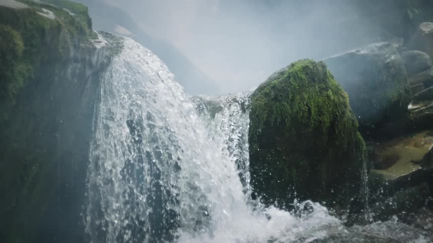 A small waterfall with lots of water hitting a large rock full of moss