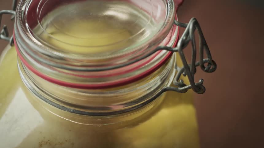 A persons hand opening a glass jar with a dense yellow liquid inside