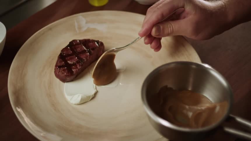 Chef adds sauce while plating steak