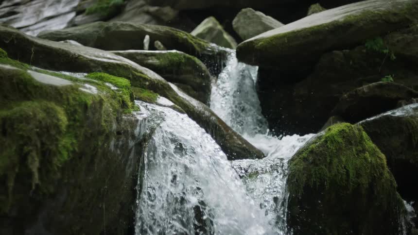 Waterfall flowing over mossy rocks in slow motion