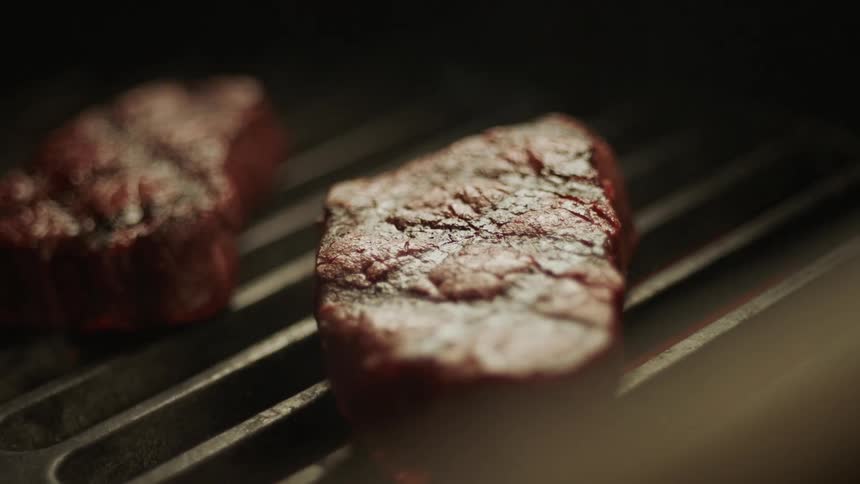 Cooking tongs placing a steak on the bbq grill