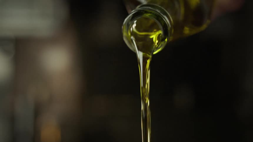 A human hand pouring a golden liquid from a transparent bottle