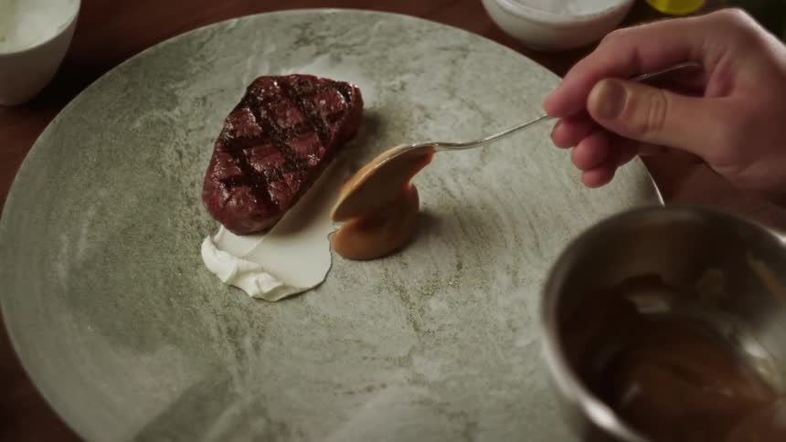 Chef adds sauce while plating grilled steak