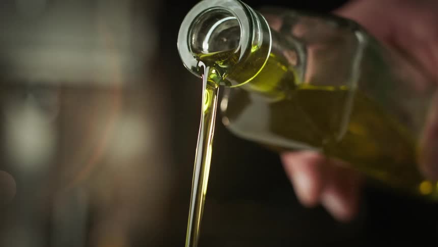 Hand holding a glass bottle and pouring olive oil in slow motion
