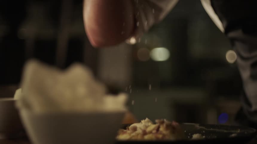 A chef sprinkles food on the dish