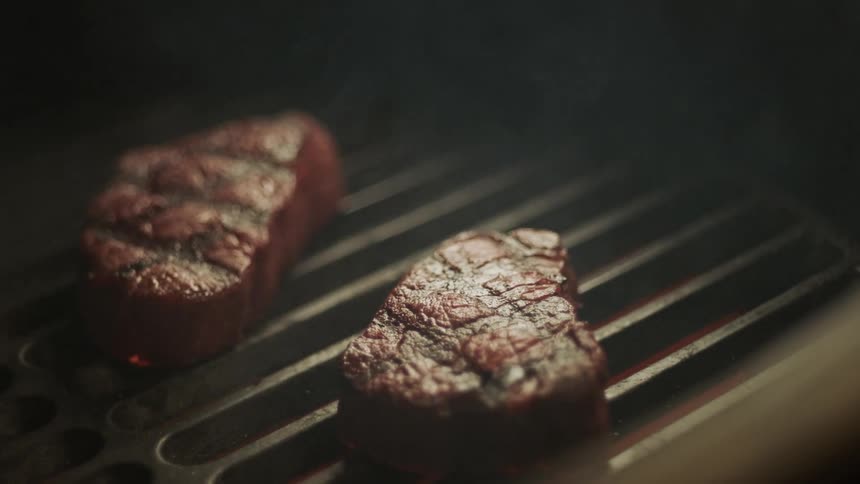 Smoke rises from steaks cooking on the grill