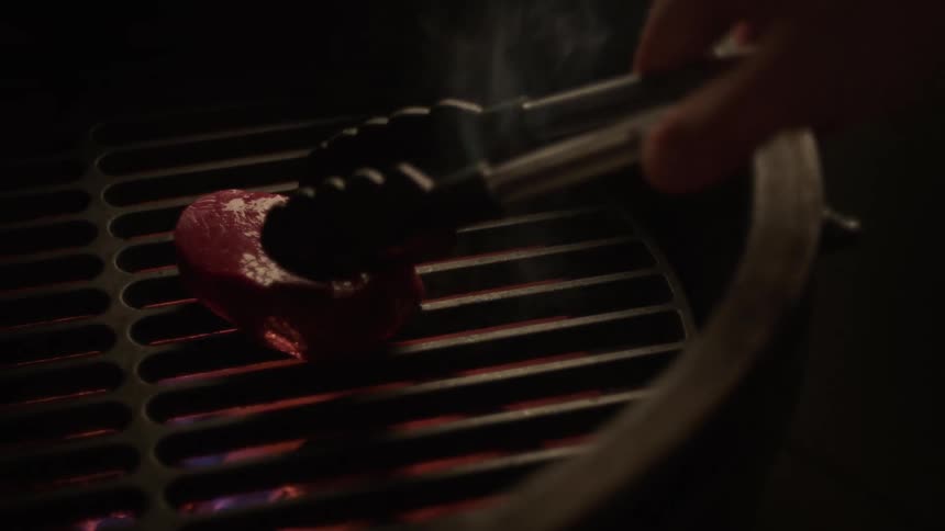 A person puts a steak on the grill