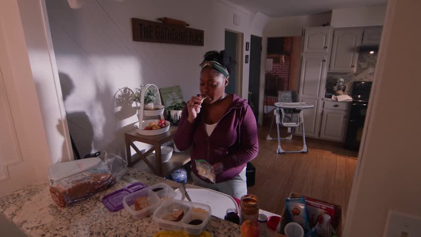 A woman prepares a meal and sneaks a snack