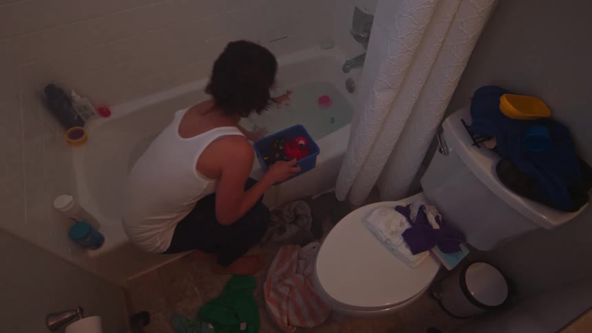 Woman in the bathroom collecting toys that are in the bathtub water and placing them in a small pot