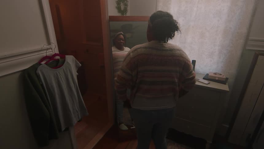 Woman inside a room trying on clothes that she is moving in front of the mirror