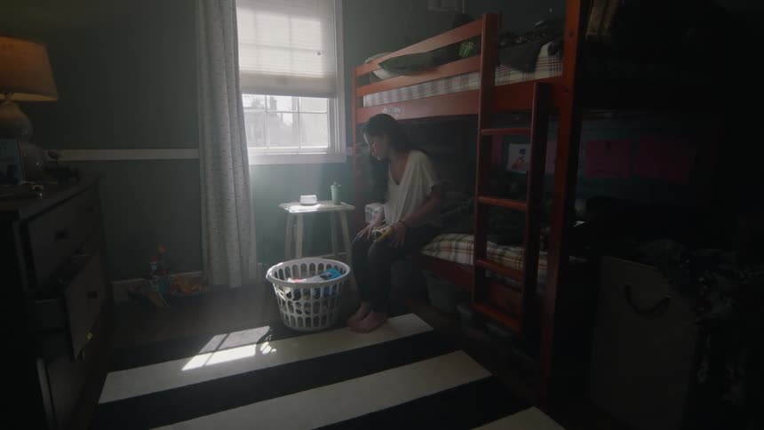 Woman entering the childrens room sitting on the bunk bed checking clothes in a basket and placing her hands on her head with a discouraged facial expression