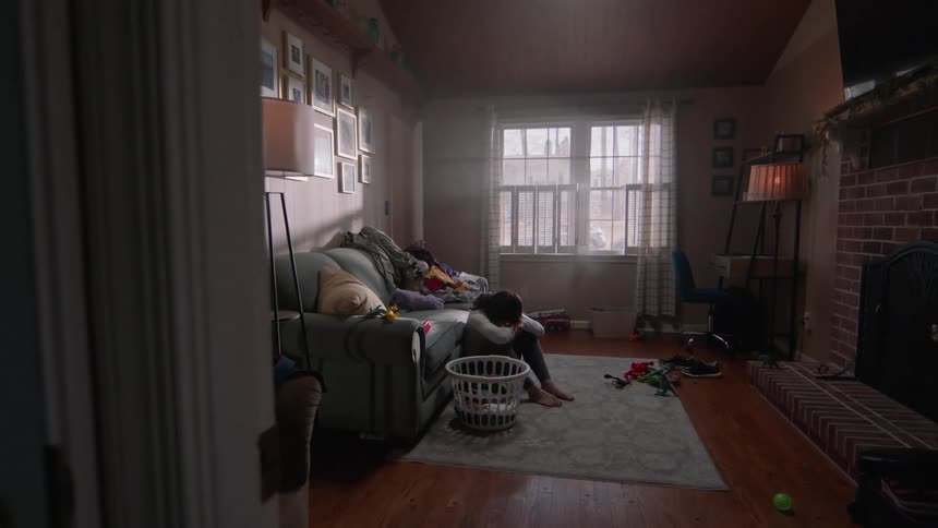 A woman is sitting in front of a sofa on the floor and is sad and putting her head between her legs