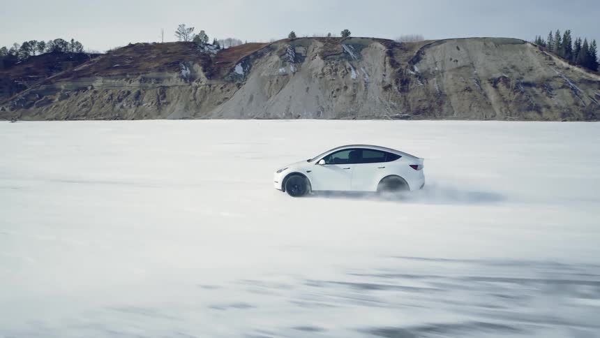 White fourdoor sports car traveling on a snowcovered ground with mountains and forests around