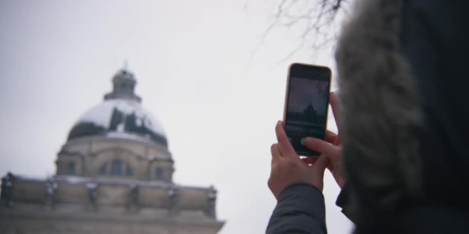 A woman uses a smart phone to take a photo of the domed tower on an old building