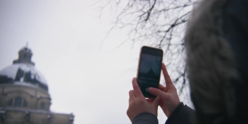 A woman uses a smart phone to take a photo of dome shaped tower from an old building