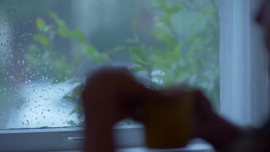 A person is drinking coffee and watching the rain outside