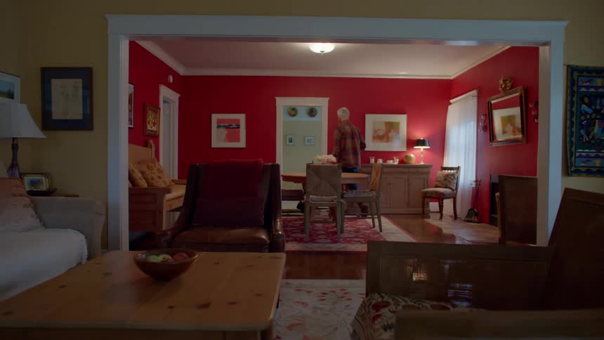 Man walking through the living room in a house with wooden furniture and artistic paintings on the walls
