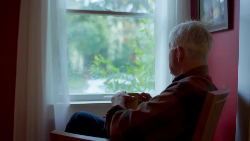 Man sitting on a chair facing the window while holding a mug