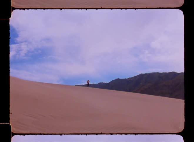 A person walking over sand dunes on a desert next to the mountains