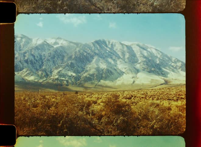 A desolate terrain with sparse vegetation next to mountains caught on vintage film