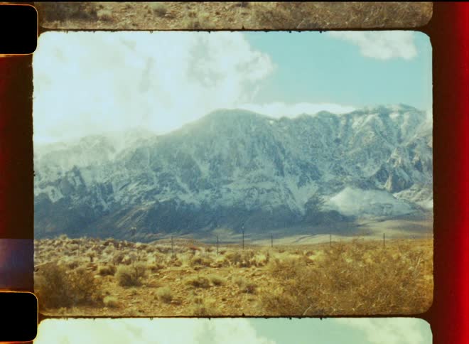 A desert valley sits at the base of a mountain range on a partly sunny day