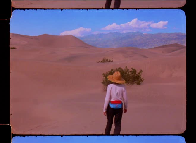 Woman walking through dunes in the desert on a blue sky day with clouds
