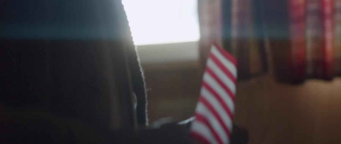 An old man paces across a room carrying a miniature American flag
