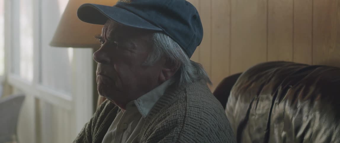 Elderly man sitting on a couch at home tears up