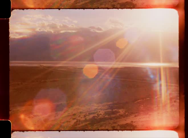 Natural landscape of a field by the sea on a clear day with clouds and a strong sun flare