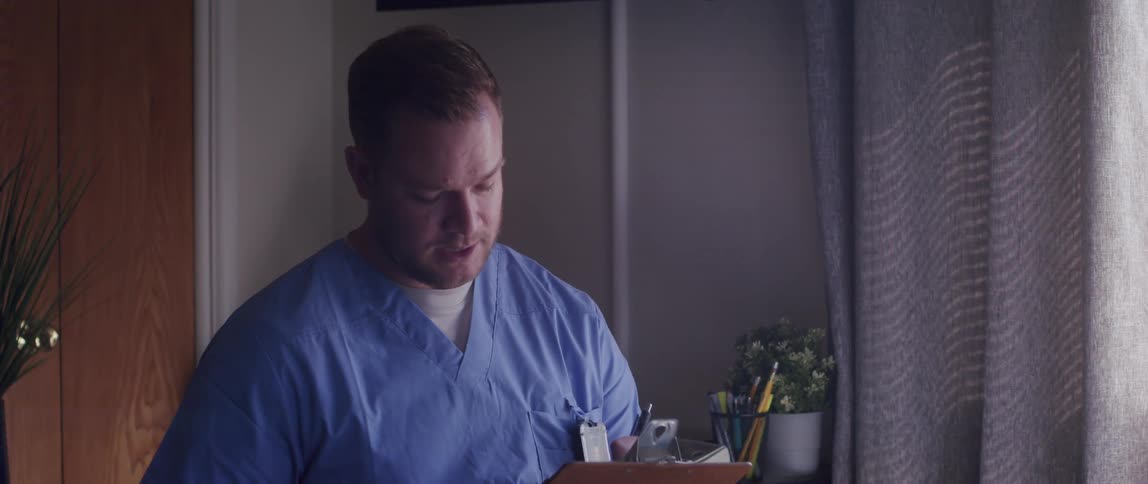 A male nurse taking notes on a clipboard