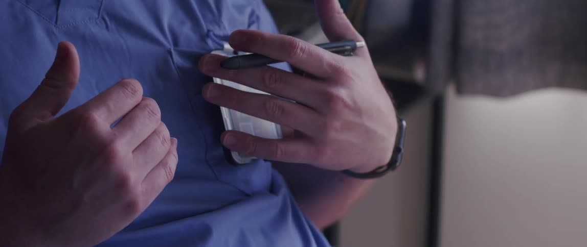 A person wearing blue medical scrubs gestures with their hands while talking