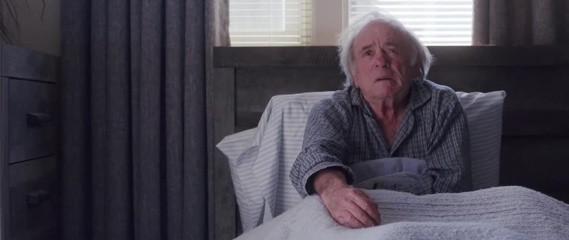 Doctor shaking hands with an elderly man who is lying on a bed with a terrified facial expression
