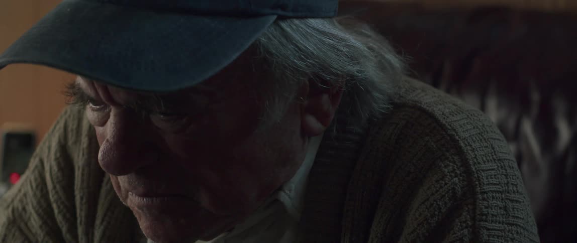Portrait of an elderly man placing his hands on his face and talking with a dejected facial expression while sitting indoors