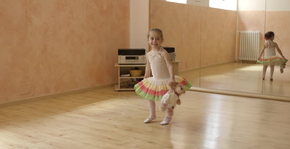 Young ballerina with a teddy bear smiling as she moves around a room