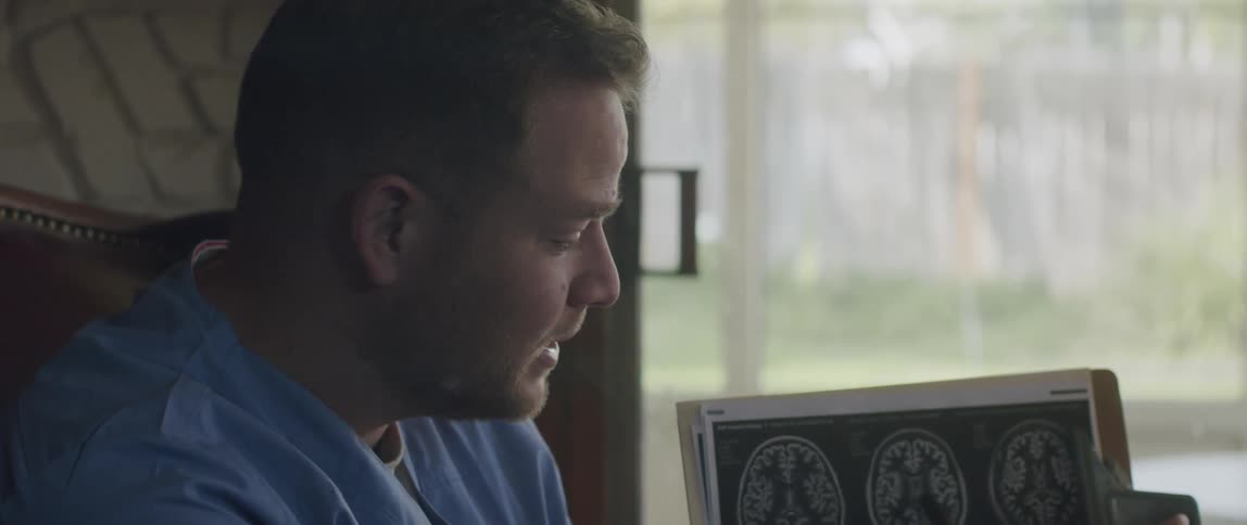 A doctor holding a chart with a ct scan using a pen to point while explaining it
