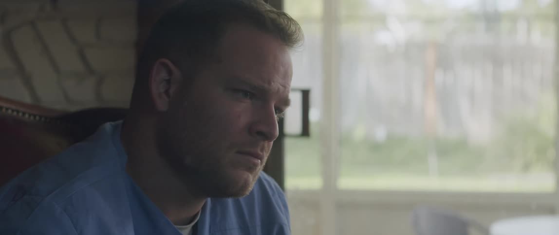 A man sits in a room listening to someone speak