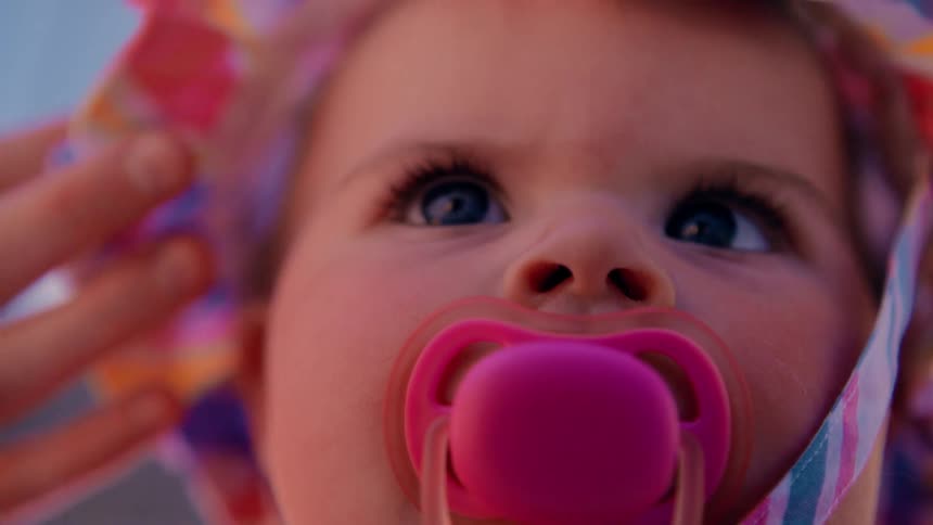 Close up of the face of a baby wearing colorful clothes and pacifier