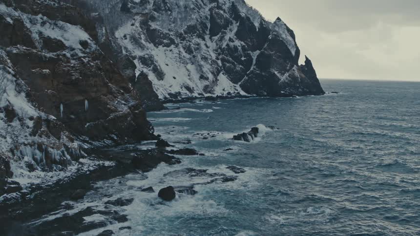 A rocky coastline with snowy mountains next to the ocean