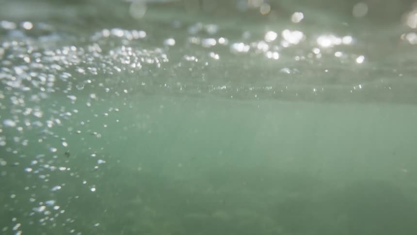 A human hand entering shallow water and causing several bubbles to rise