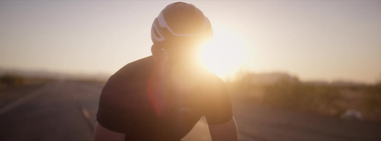 Cyclist rides his bike down the center of an empty road with mountains in the distance behind him