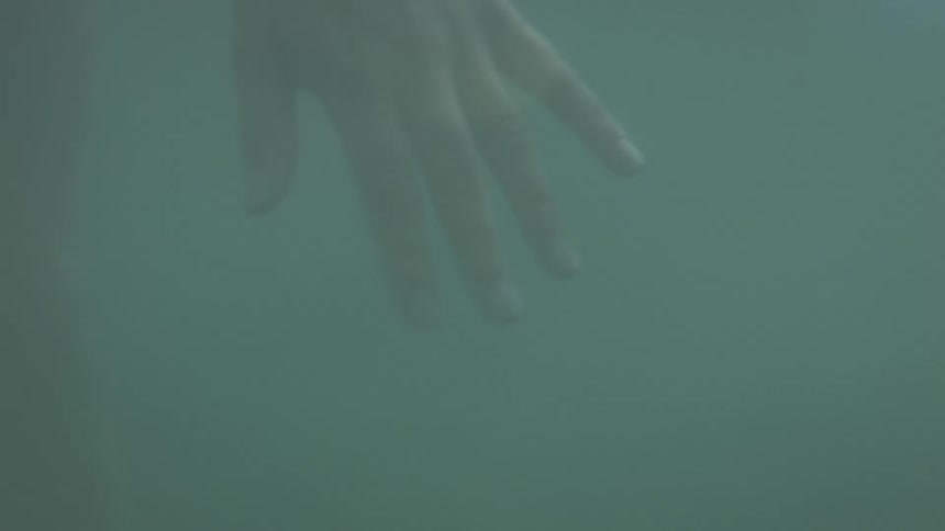A person holds their hand underwater while extending their fingers