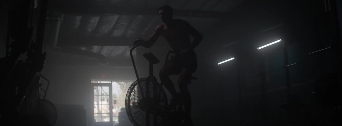Man performing cardio on an elliptical bike in lowlight environment