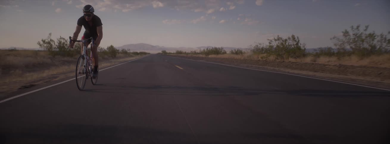 A man rides his bicycle on a rural road with mountains in the distance