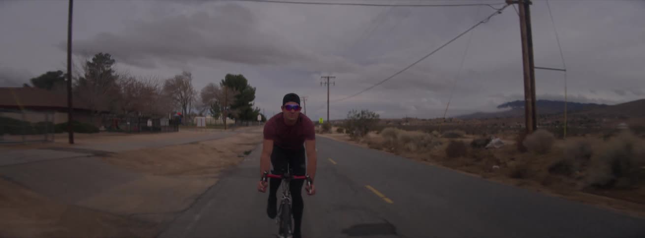 Concentrated cyclist cycling on a road in an environment with grassland around on a cloudy day