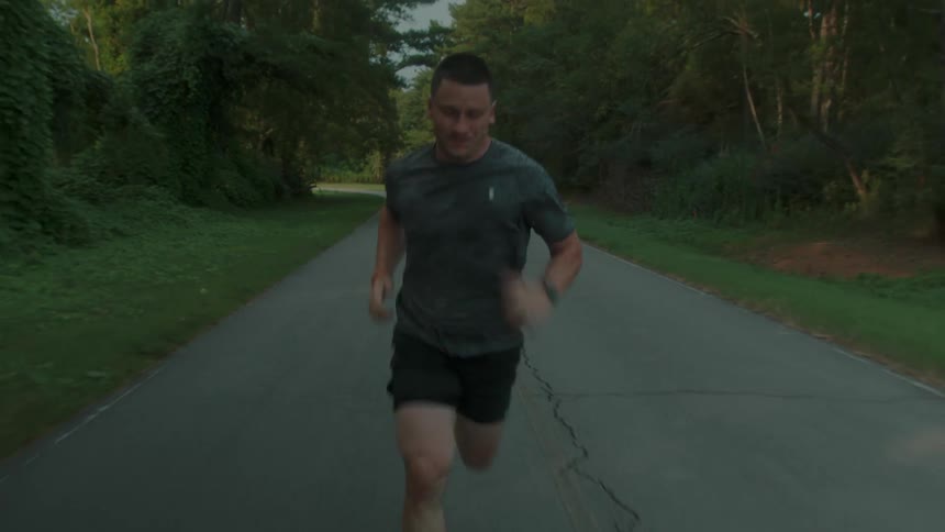 A man is running hard and fast on a road surrounded by trees and woods