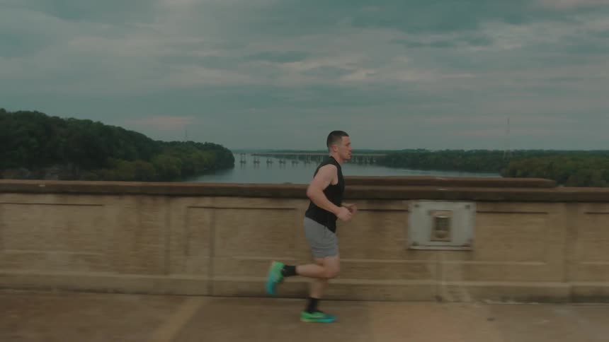 A man jogging on a bridge crossing a river