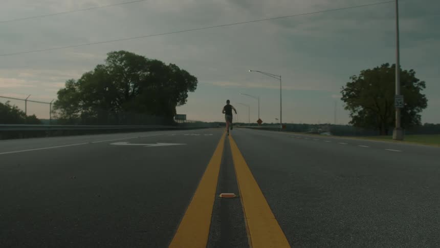A man in running gear jogging on the double yellow line of an empty street
