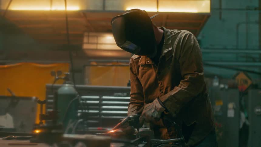 A welder wearing a face shield uses a welding torch in a workshop